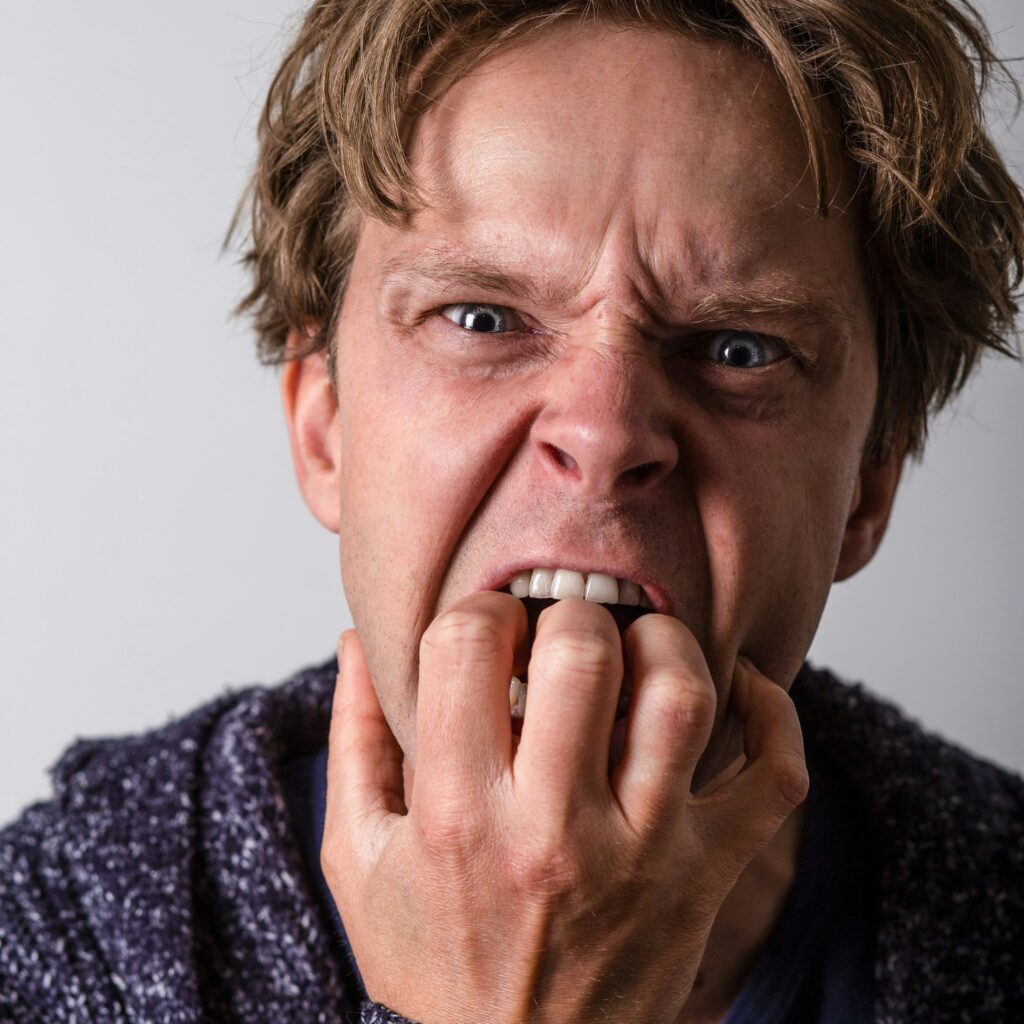 Angry man with curled fingers clutched in his mouth and a furled brow - livid with frustration